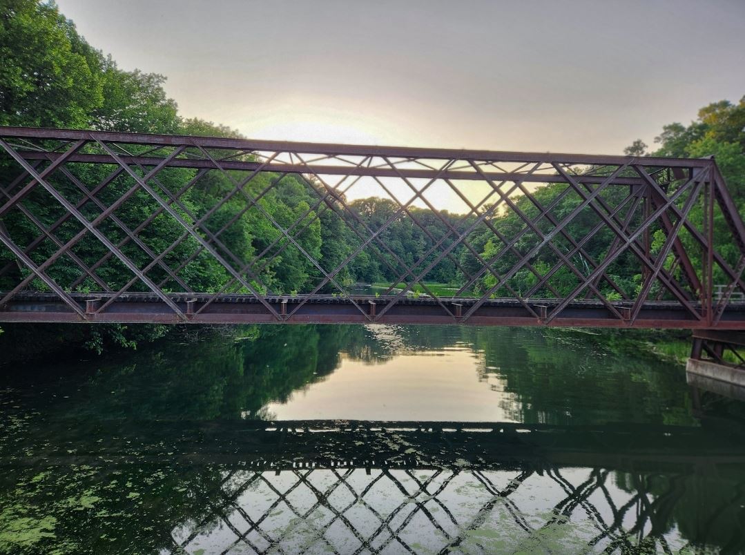 A bridge over a river that is surrounded by green trees.